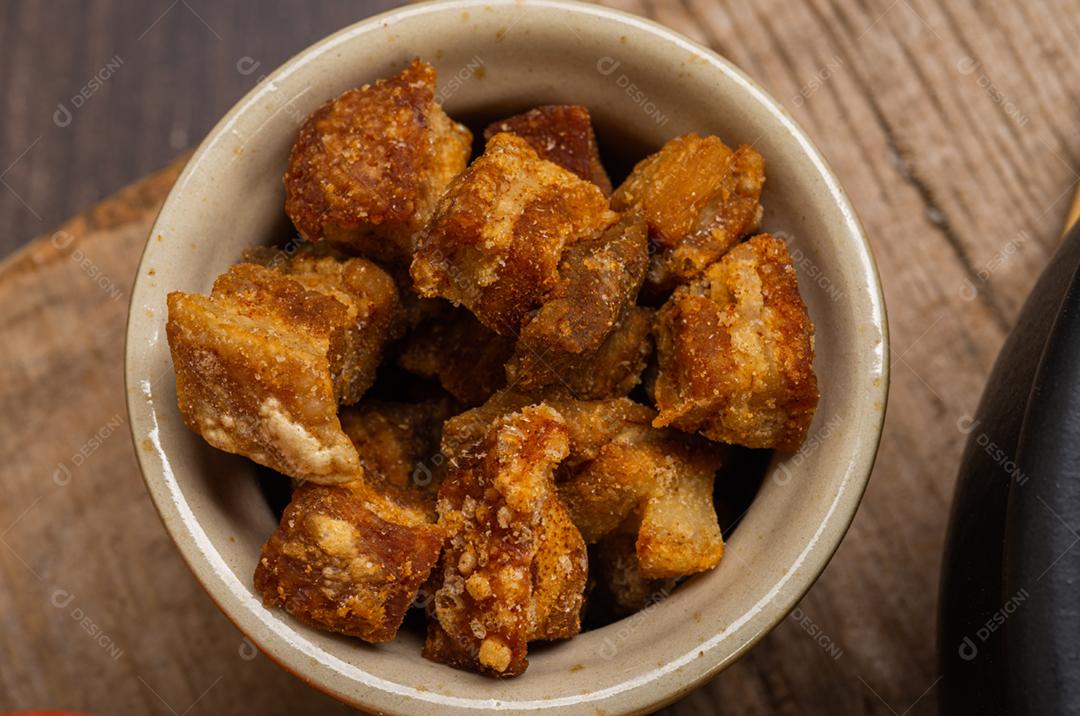 Torresmos fritos servidos em uma tigela de barro em uma mesa de madeira rústica