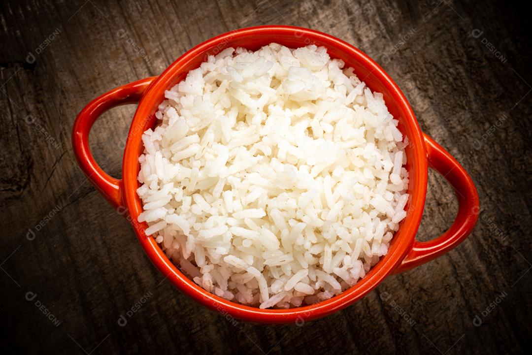 Arroz branco servido em uma tigela de barro em uma mesa de madeira rústica