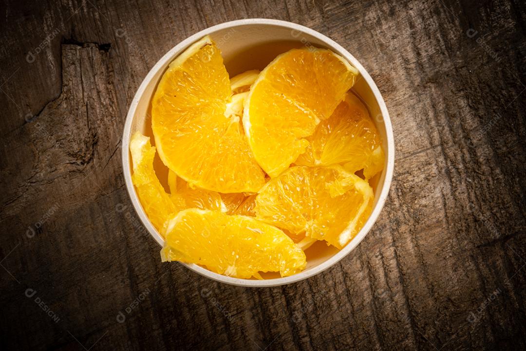 Fatias de laranja servidas em uma tigela de barro na mesa de madeira rústica