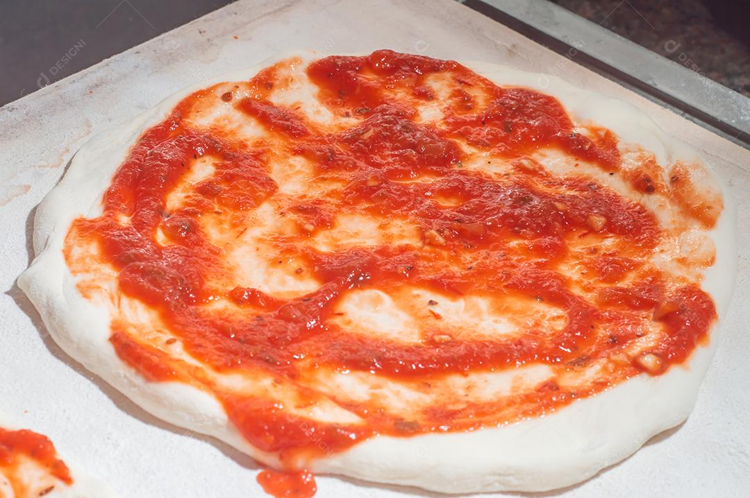 Massa de pizza com molho de tomate sendo colocado e queijo mussarela, conceito de pizza.