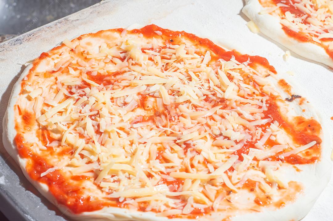 Massa de pizza com molho de tomate sendo colocado e queijo mussarela, conceito de pizza.