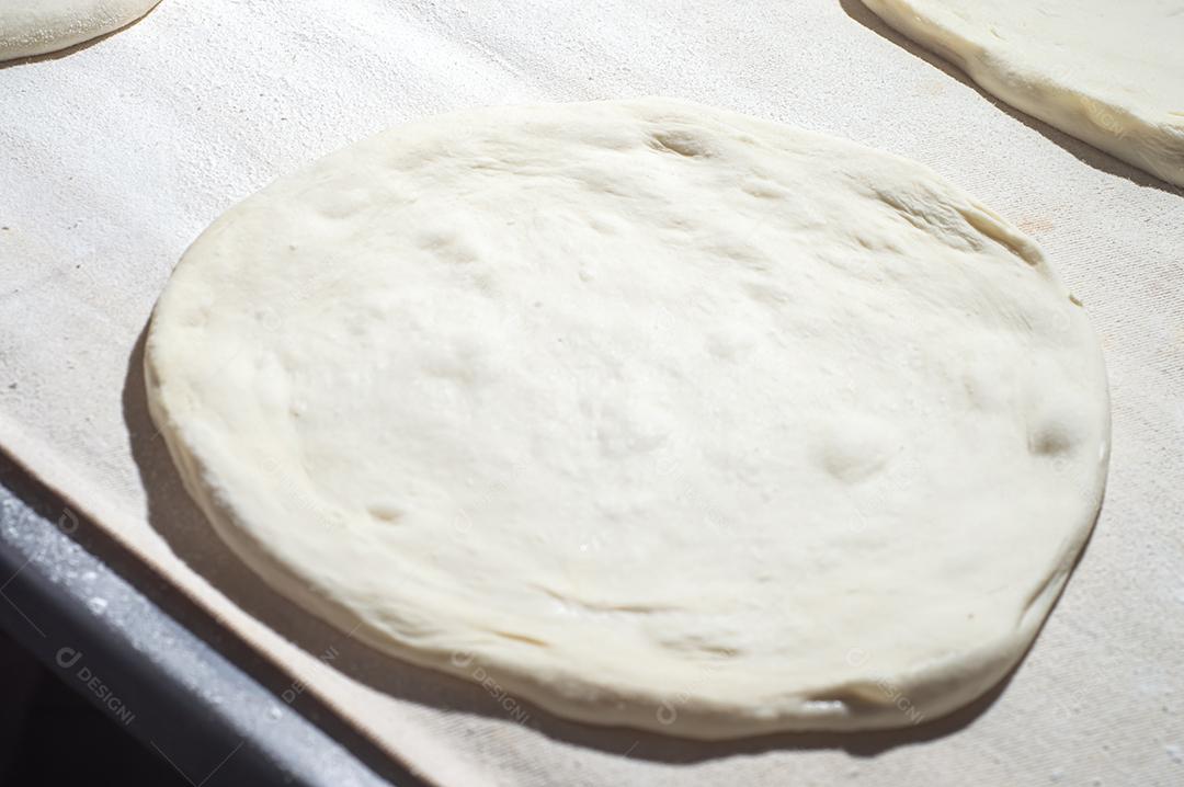 Massa de pizza em uma mesa branca com luz dura.