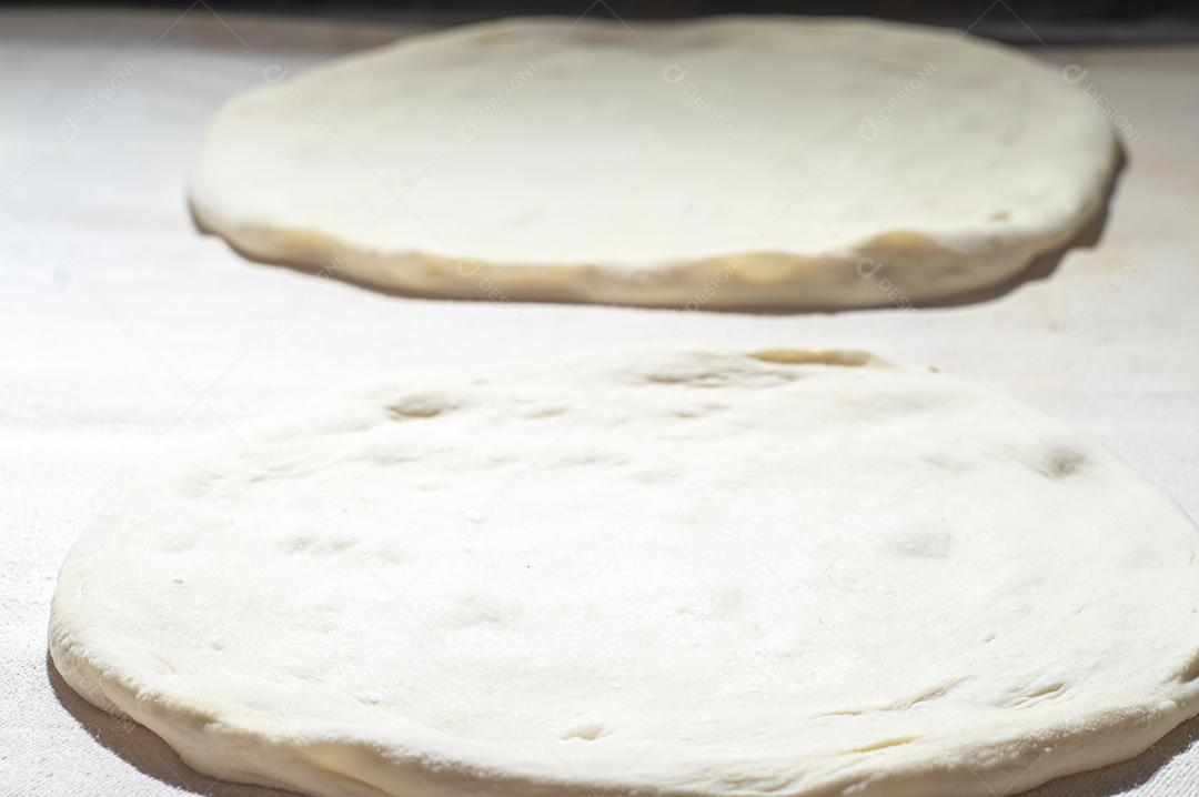 Massa de pizza em uma mesa branca com luz dura.