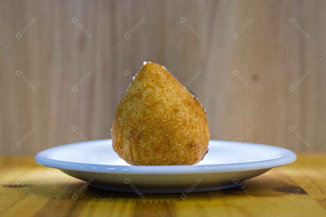 Coxinha em prato branco sobre mesa de madeira