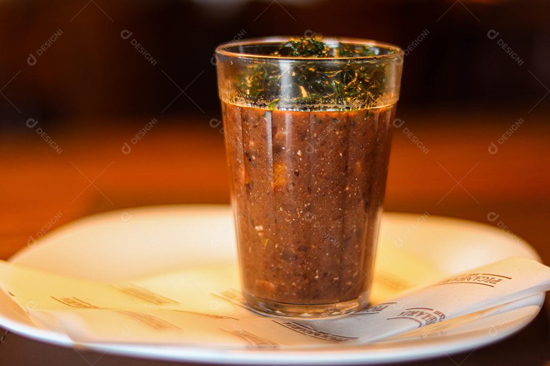 Copo de vidro com temperos e pimentas acima de prato