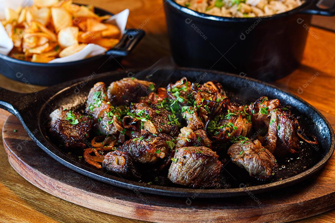 Panela preta com carnes temperadas em cima de mesa de madeira