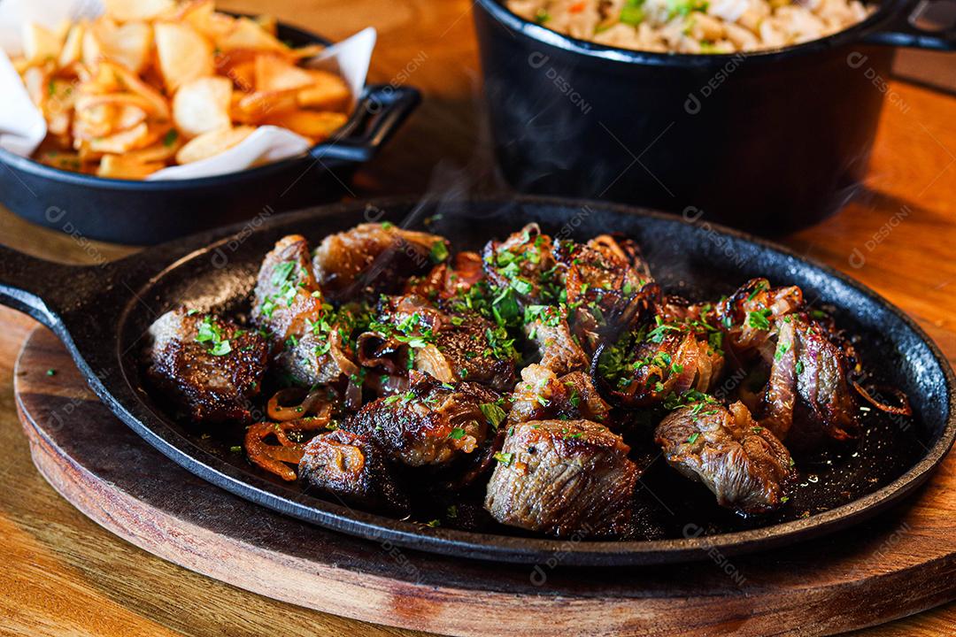 Panela preta com carnes temperadas em cima de mesa de madeira