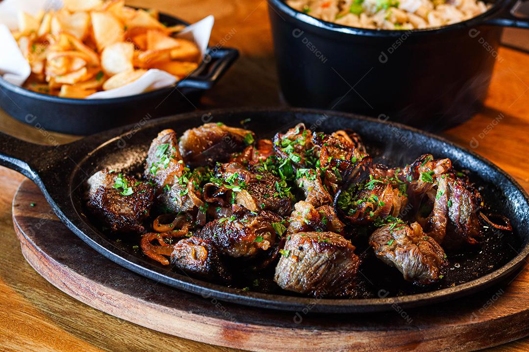 Panela preta com carnes temperadas em cima de mesa de madeira