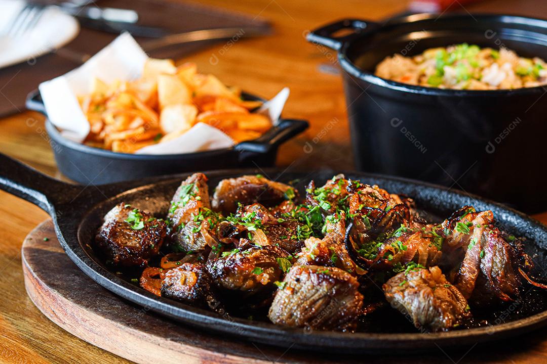 Panela preta com carnes temperadas em cima de mesa de madeira