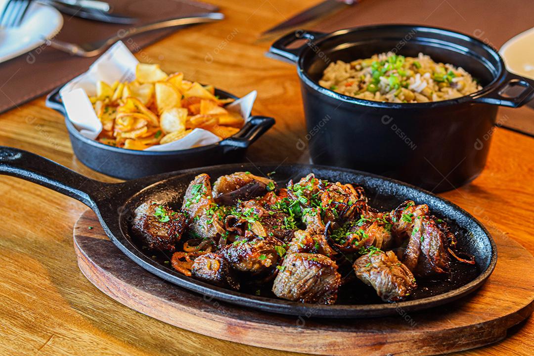 Panela preta com carnes temperadas em cima de mesa de madeira