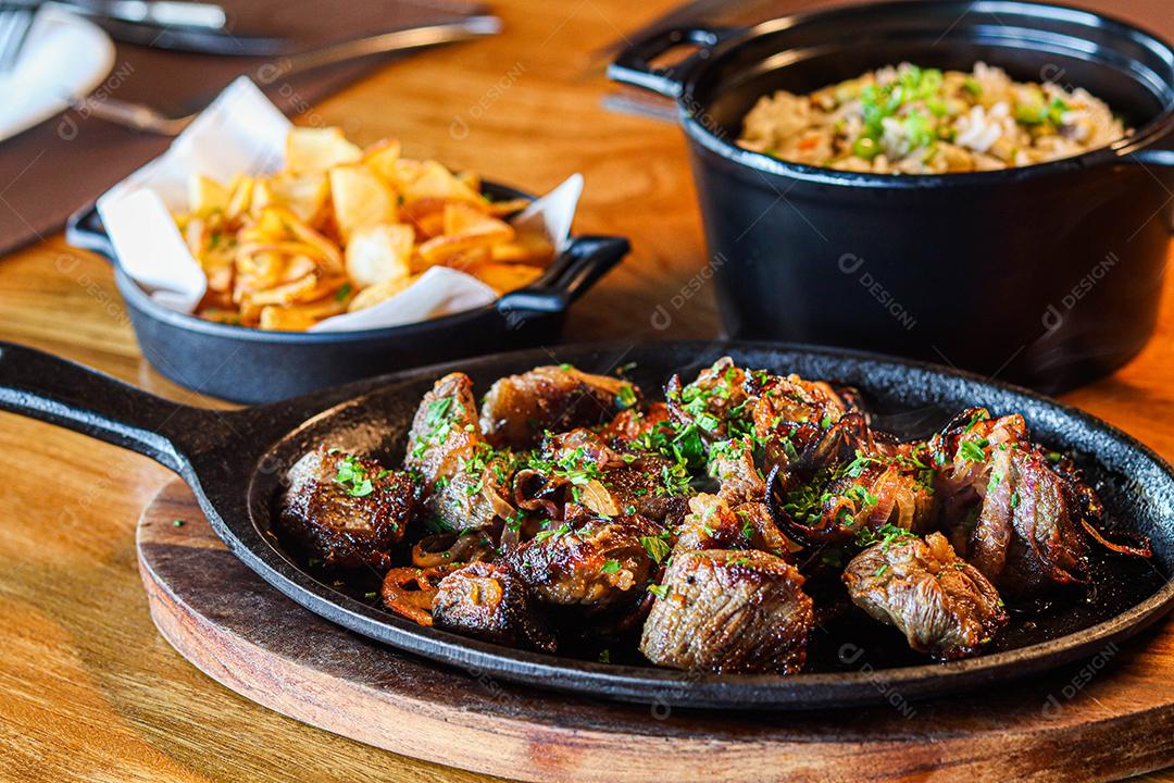 Panela preta com carnes temperadas em cima de mesa de madeira