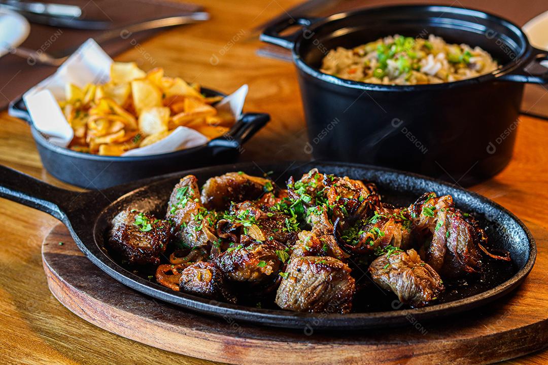 Panela preta com carnes temperadas em cima de mesa de madeira