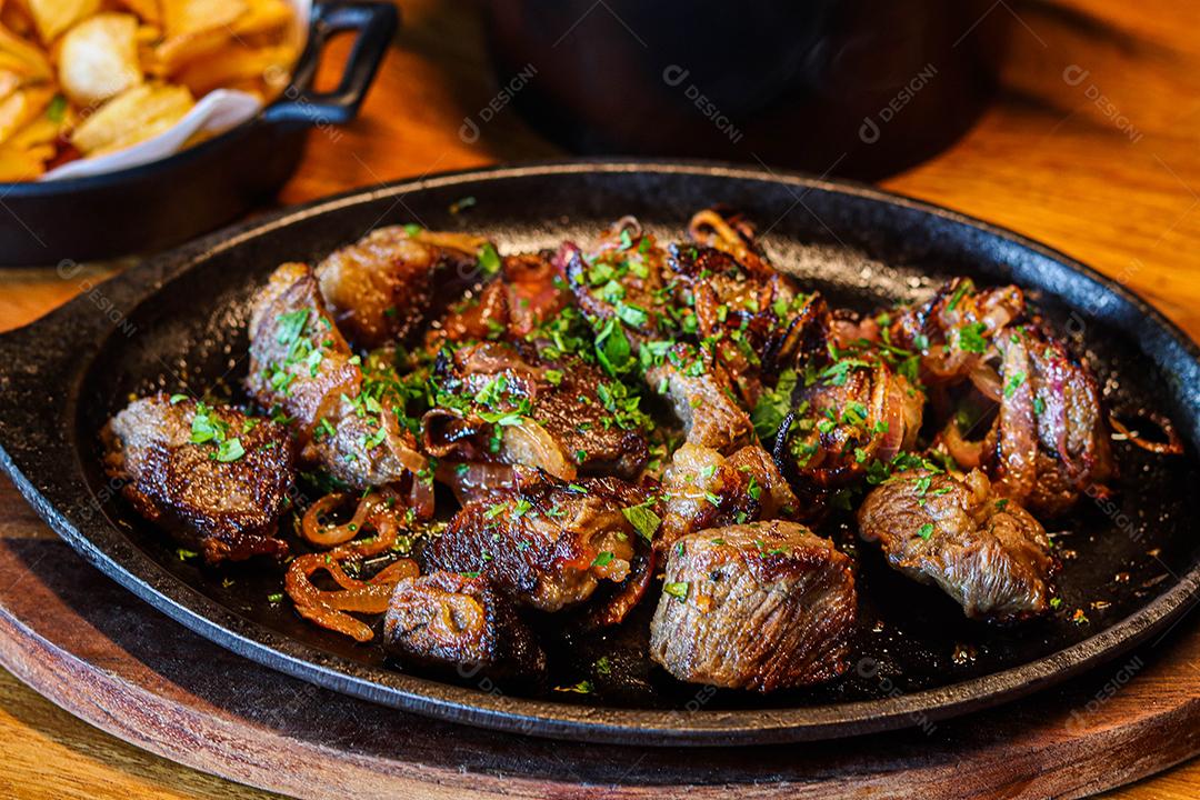 Panela preta com carnes temperadas em cima de mesa de madeira