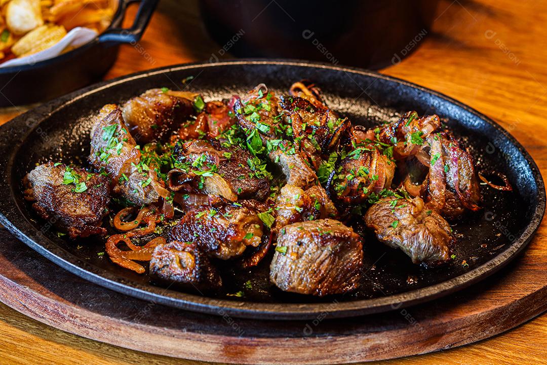 Panela preta com carnes temperadas em cima de mesa de madeira
