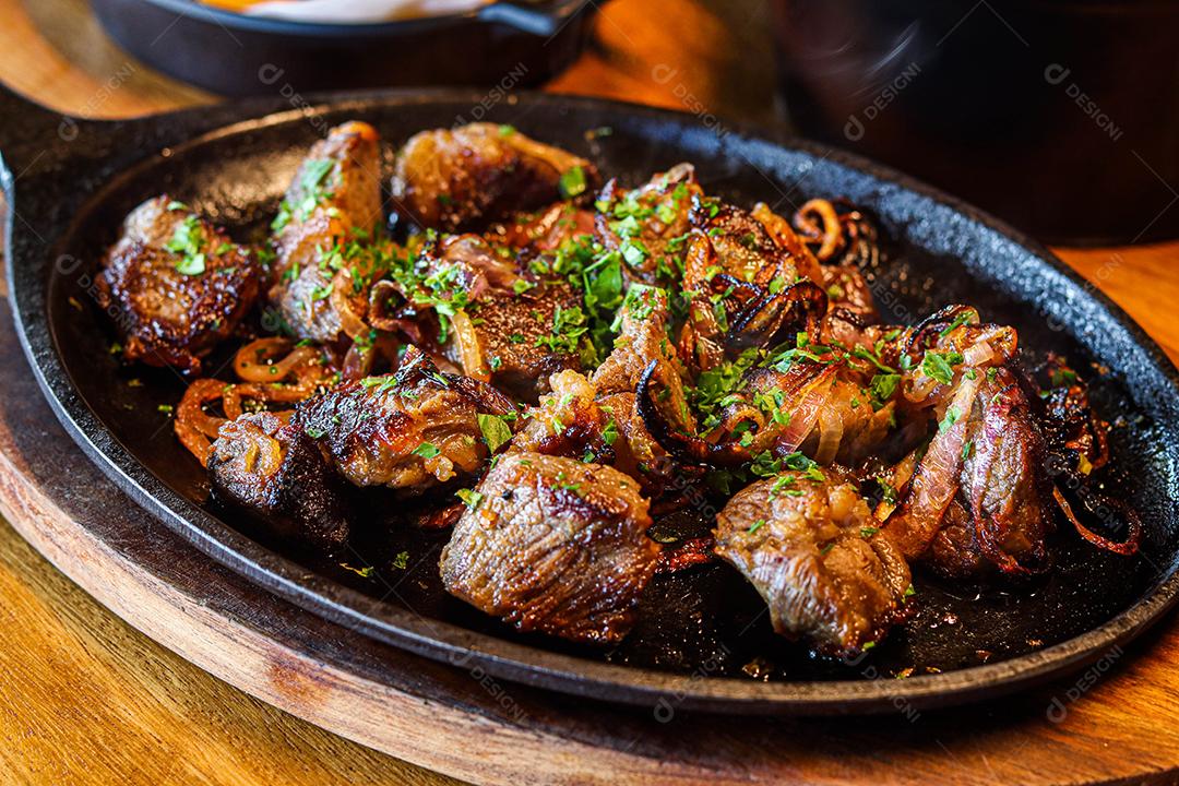 Panela preta com carnes temperadas em cima de mesa de madeira