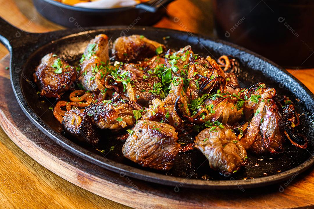 Panela preta com carnes temperadas em cima de mesa de madeira