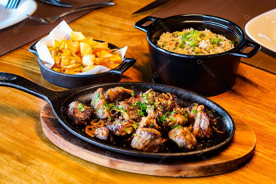 Panela preta com carnes temperadas em cima de mesa de madeira