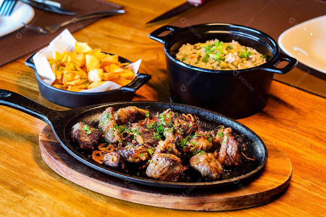 Panela preta com carnes temperadas em cima de mesa de madeira
