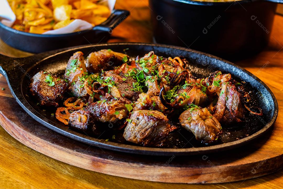 Panela preta com carnes temperadas em cima de mesa de madeira