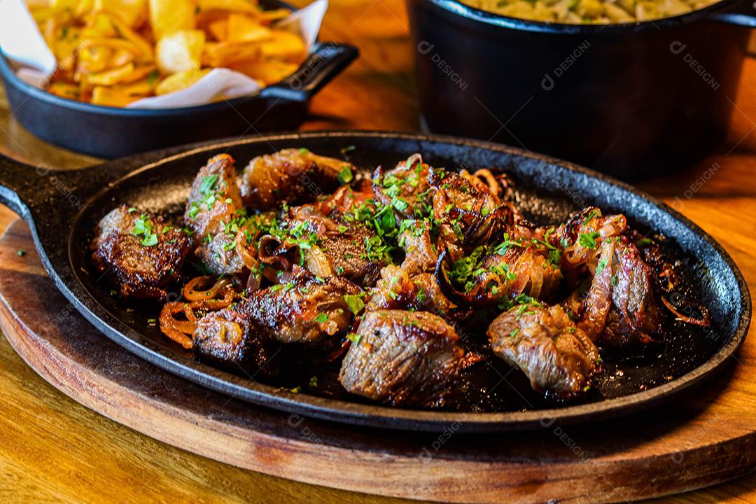 Panela preta com carnes temperadas em cima de mesa de madeira