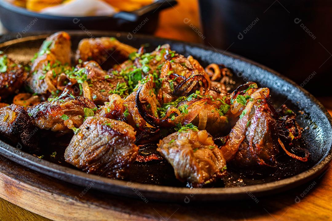 Panela preta com carnes temperadas em cima de mesa de madeira