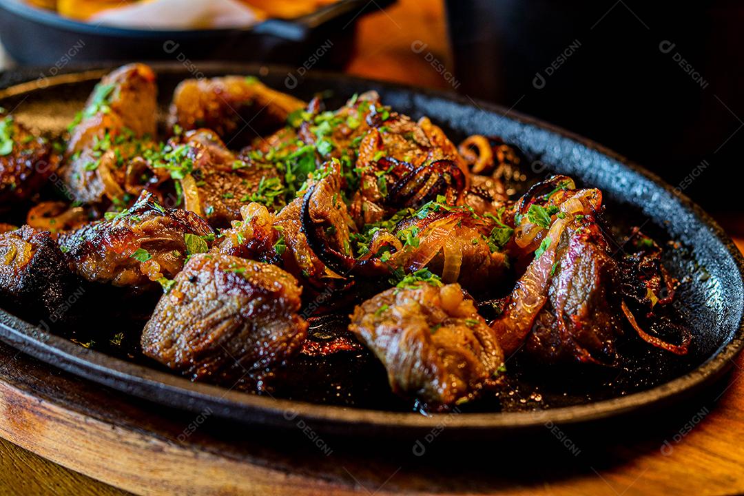 Panela preta com carnes temperadas em cima de mesa de madeira