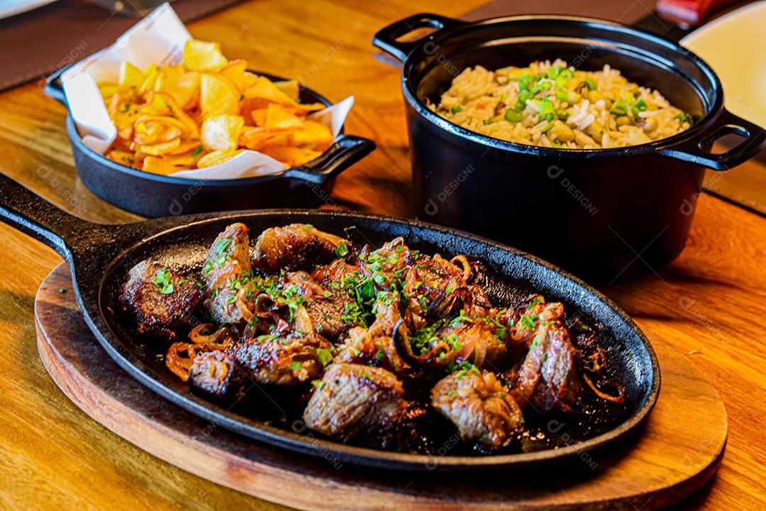 Panela preta com carnes temperadas em cima de mesa de madeira