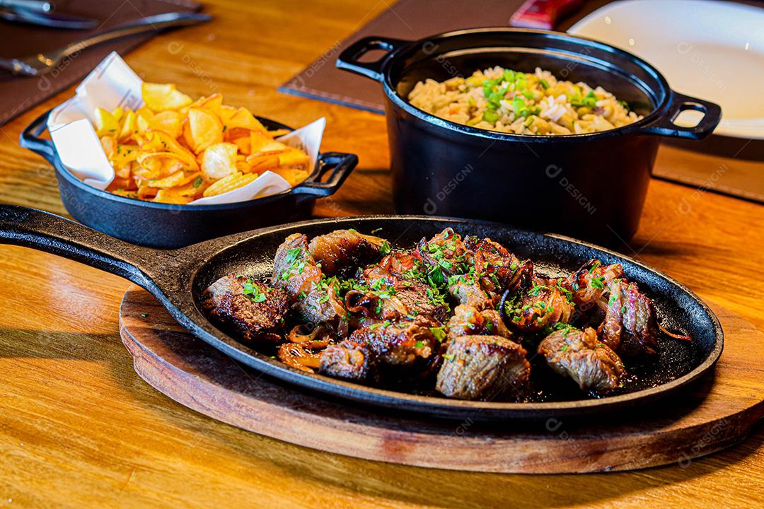 Panela preta com carnes temperadas em cima de mesa de madeira