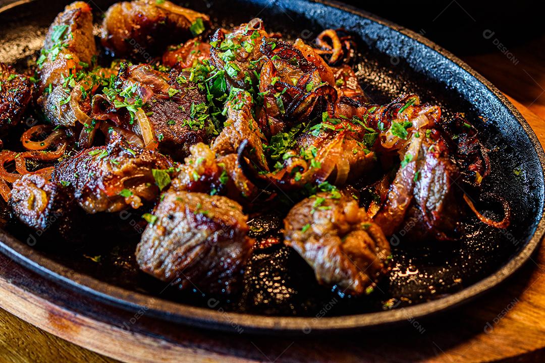 Panela preta com carnes temperadas em cima de mesa de madeira