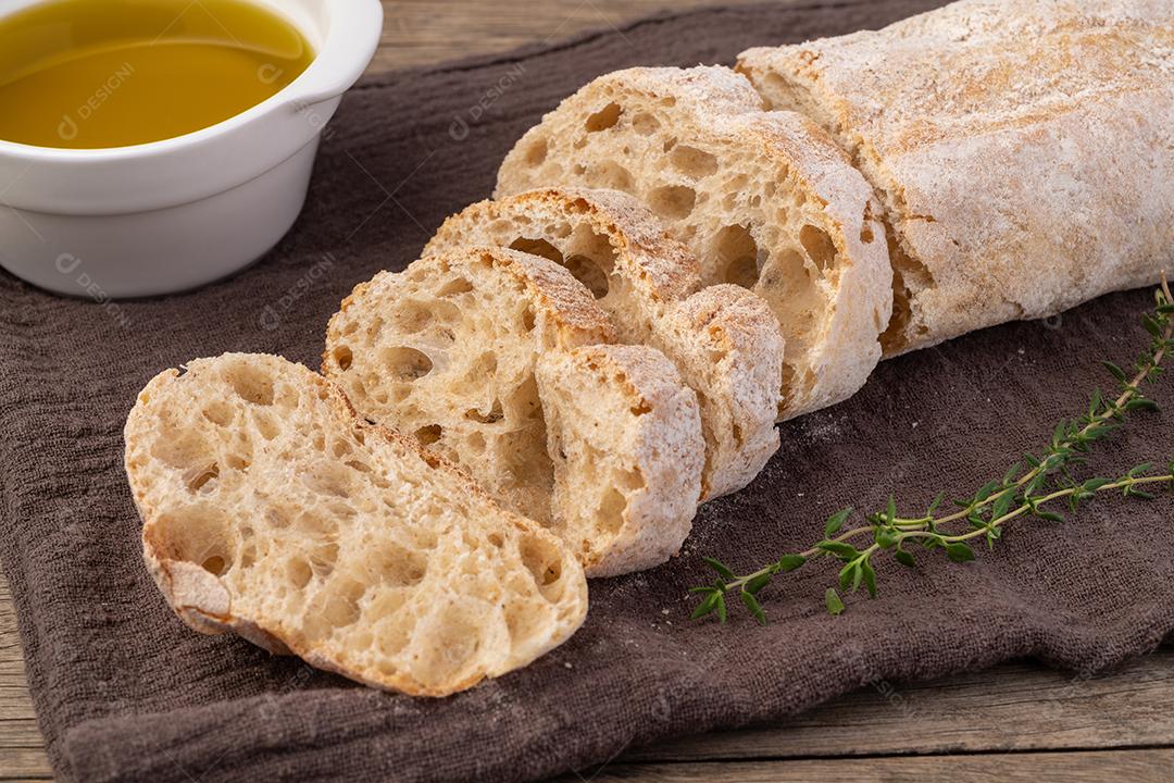 Pão ciabatta caseiro tradicional com fatias e azeite sobre a mesa de madeira.