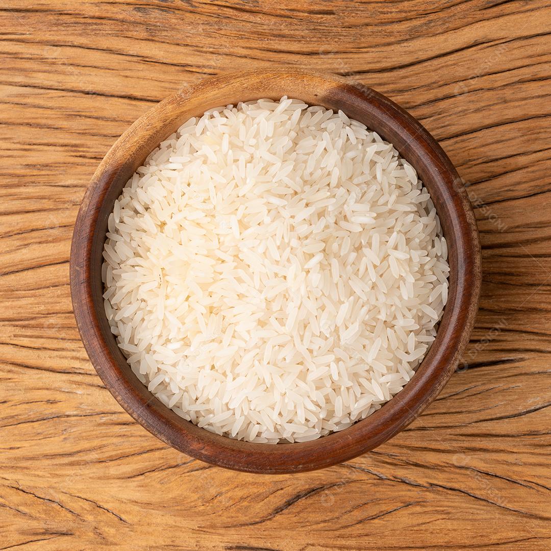 Arroz branco cru em uma tigela sobre a mesa de madeira.