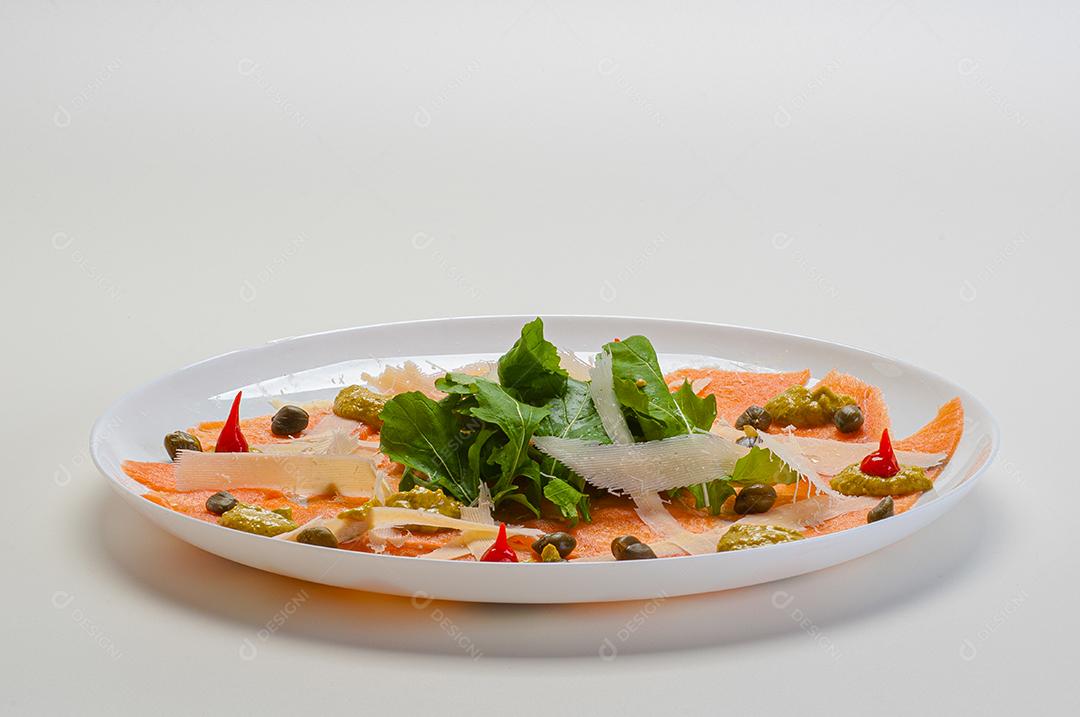 Carpaccio de salmão servido com rúcula e alcaparras.