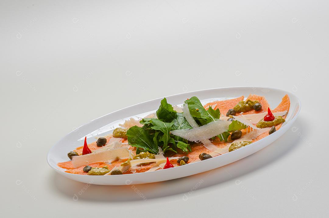 Carpaccio de salmão servido com rúcula e alcaparras.