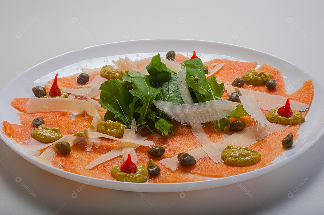 Carpaccio de salmão servido com rúcula e alcaparras.