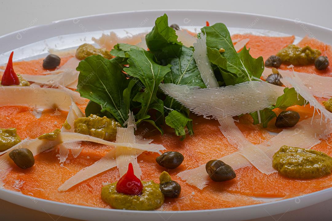 Carpaccio de salmão servido com rúcula e alcaparras.