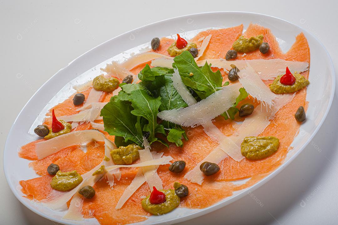 Carpaccio de salmão servido com rúcula e alcaparras.