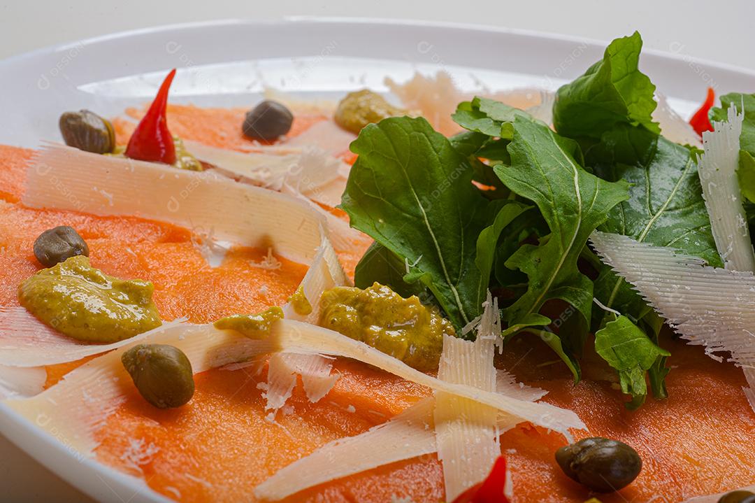 Carpaccio de salmão servido com rúcula e alcaparras.