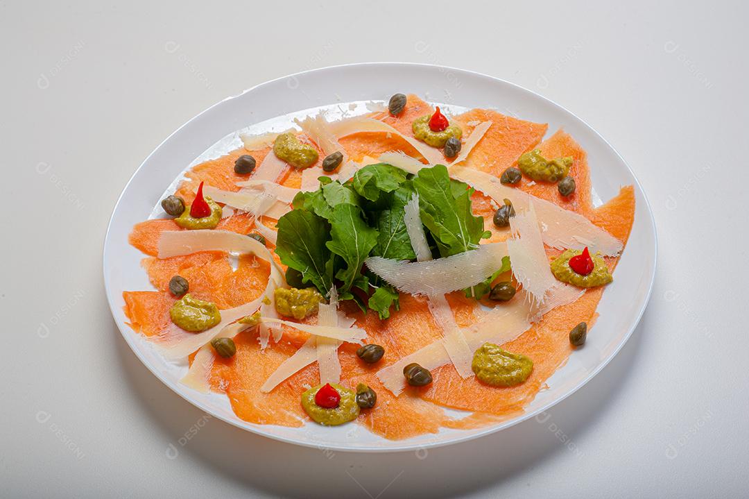 Carpaccio de salmão servido com rúcula e alcaparras.