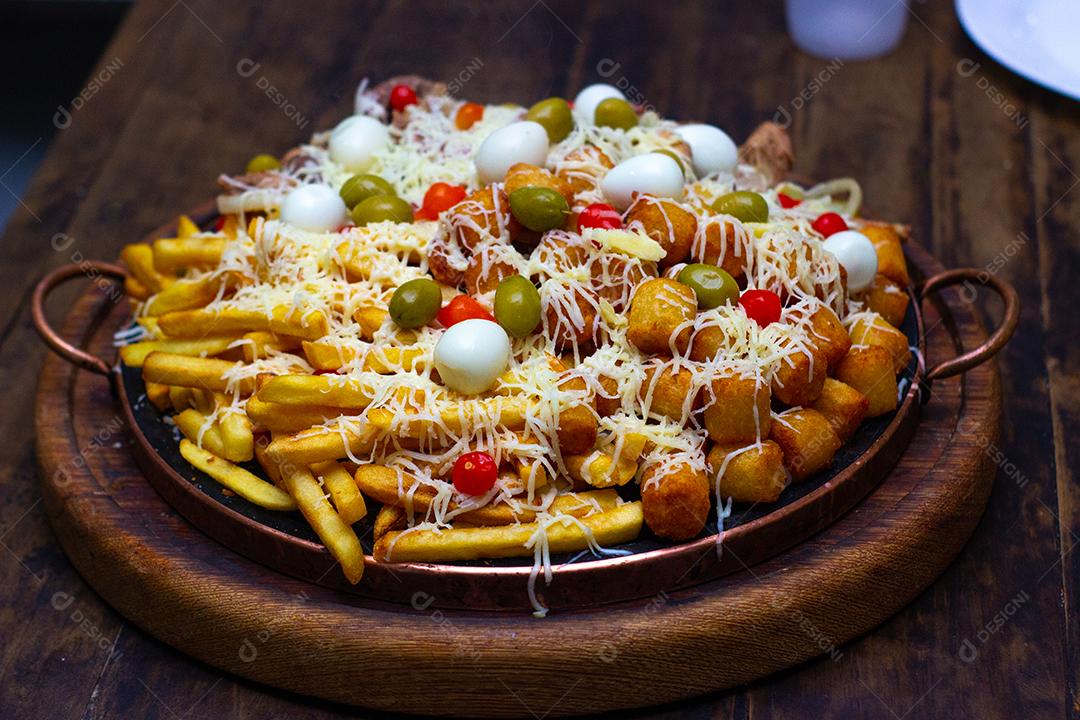 Comida típica com ovos, tomate, azeitona, salgados, cebola, queijo, bacon, calabresa, batata frita, carne sobre placa de madeira