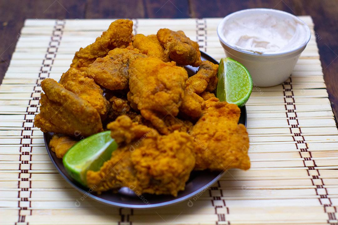 Frango frito com creme e limão sobre mesa madeira.