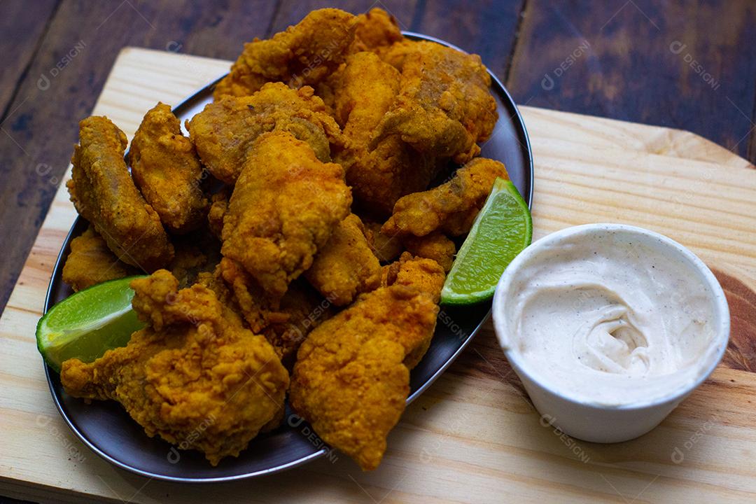 Frango frito, creme branco e limão sobre placa de madeira.
