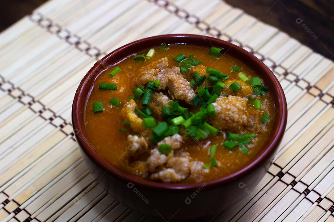 Sopa de bacon com milho e cebolinha verde em uma tigela sobre mesa madeira.