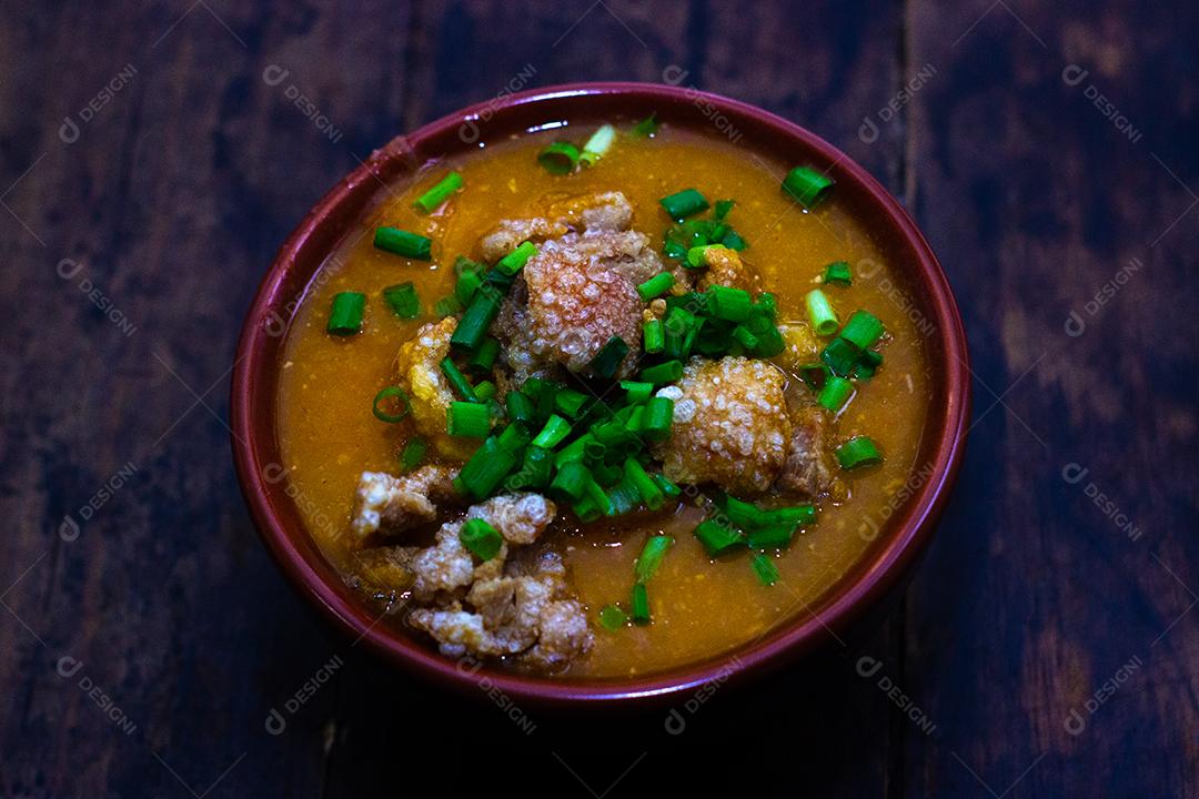 Sopa de bacon com milho e cebolinha verde em uma tigela sobre mesa madeira.