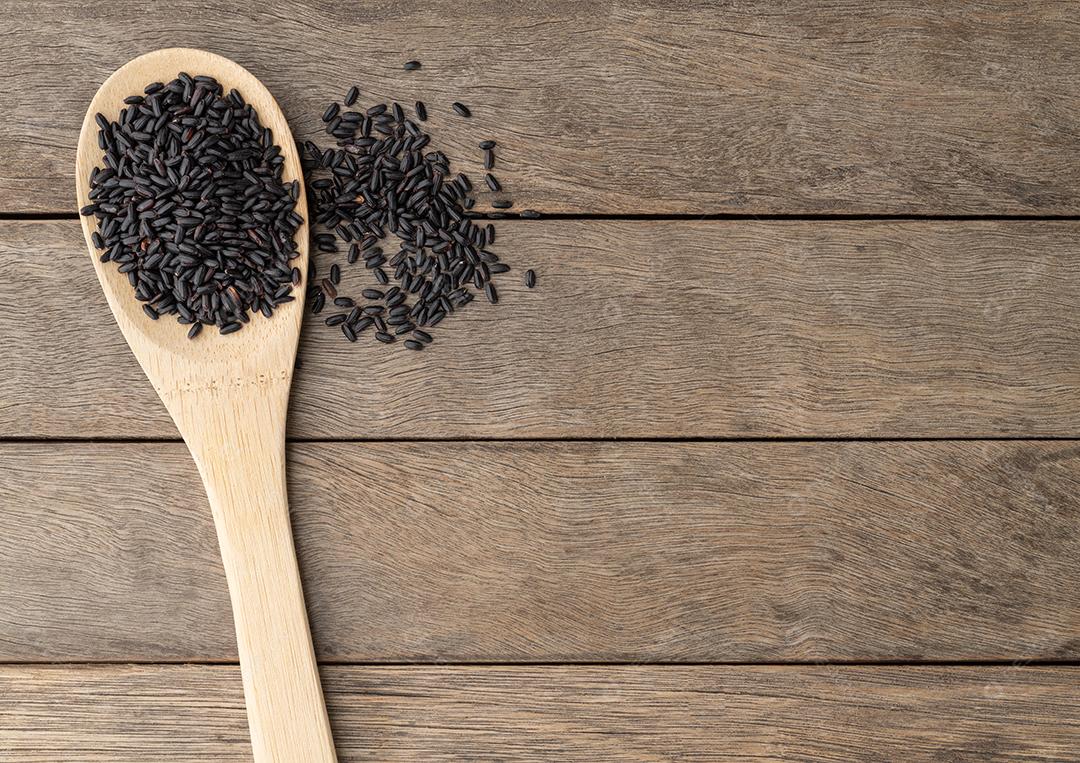 Arroz preto cru em uma colher sobre a mesa de madeira