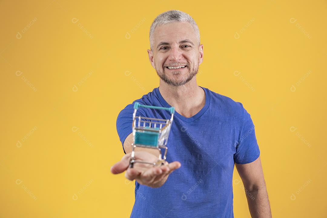 Homem de meia idade segurando um mini carrinho de compras