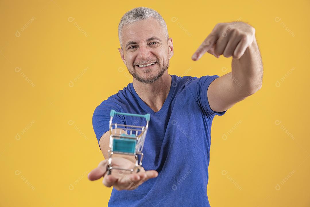 Homem de meia idade segurando um mini carrinho de compras