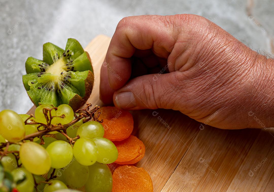 Homem organizando uma tábua de frutas com uva verde, damasco, morango