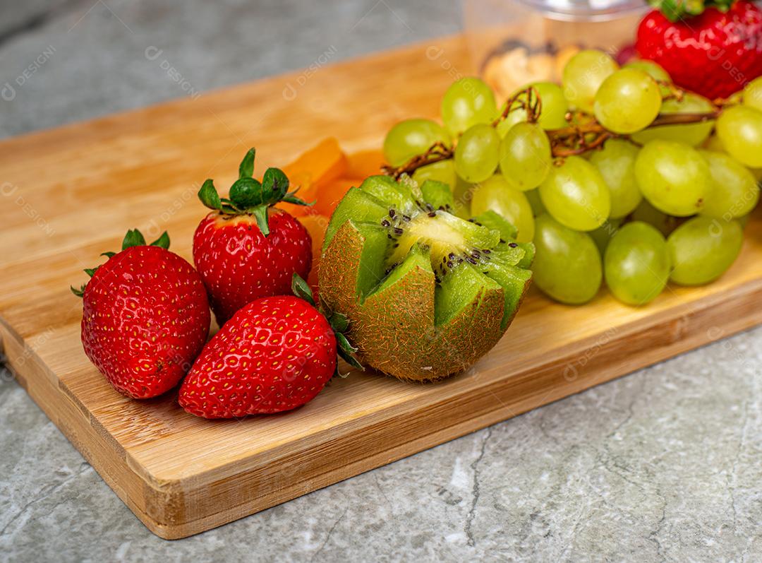 Tábua de madeira rústica decorada com frutas (morangos, kiwi, damasco e uvas verdes) em pedra mármore.