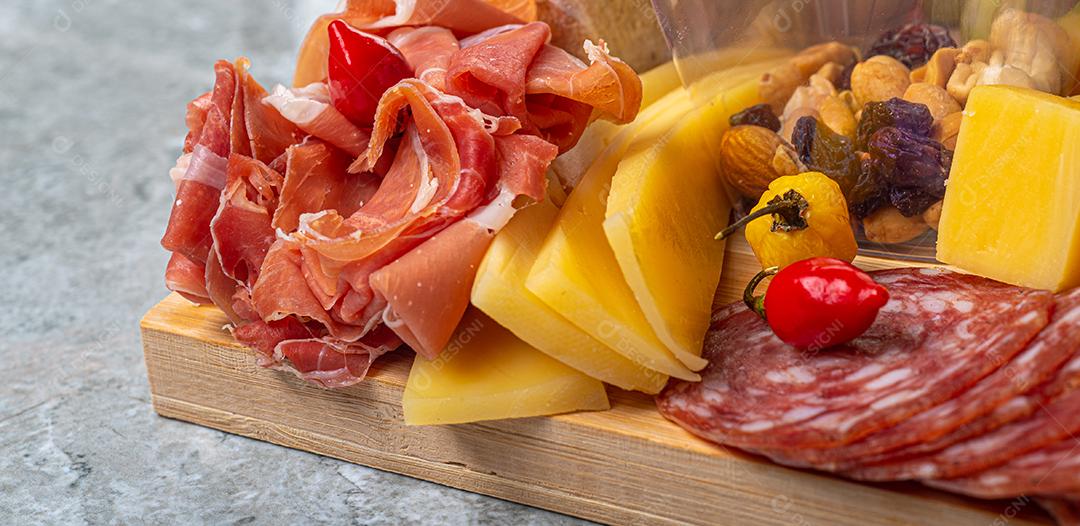 Tábua de frios e frutas servida em fundo de madeira e mármore com queijo, presunto, salame marrom, morangos, kiwis