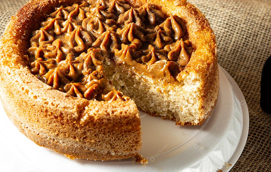 bolo de churros típico brasileiro com doce de leite com uma fatia cortada, em uma mesa com pratos e café, cena confortável de café da manhã ou lanche. tiro de perto